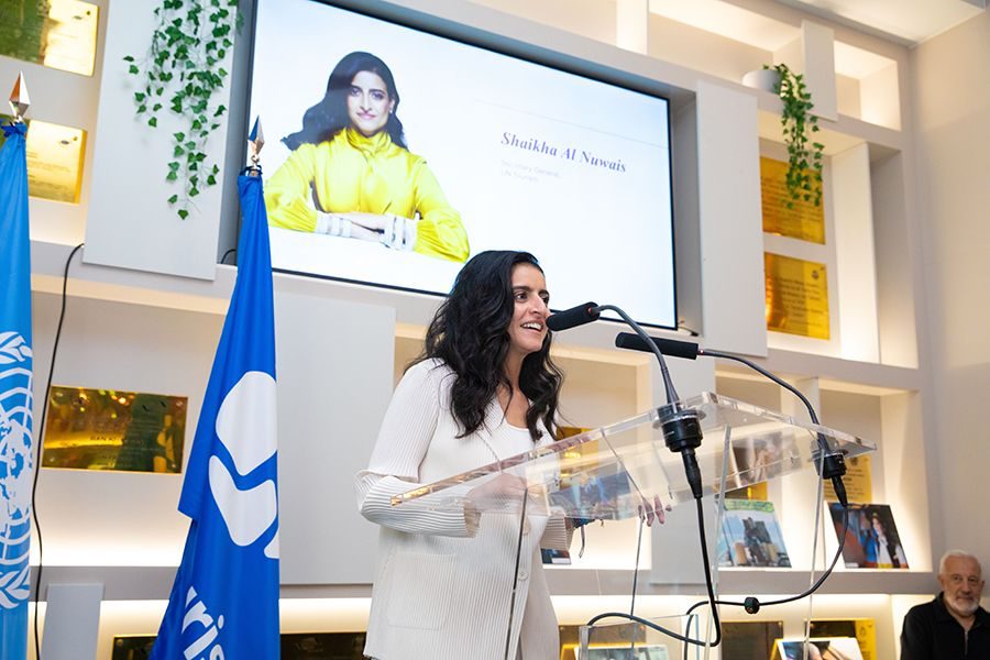 Woman speaker at podium with UN flag, addressing audience about women in tourism transport