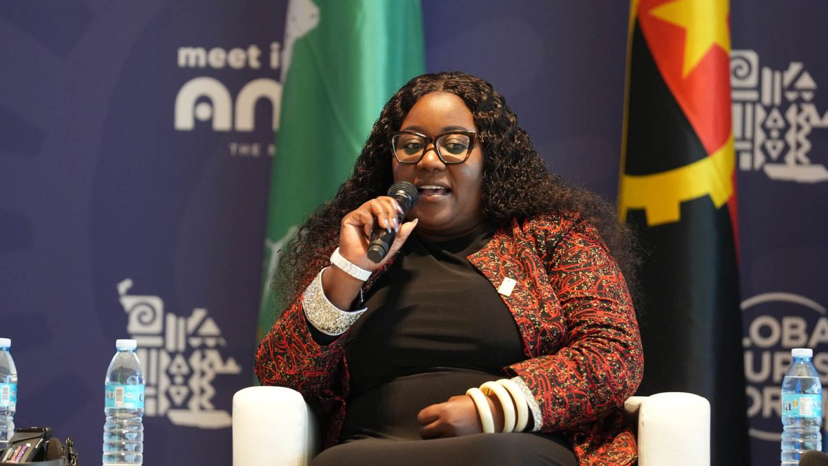 Woman speaking at MICE conference panel with Angola flags in background