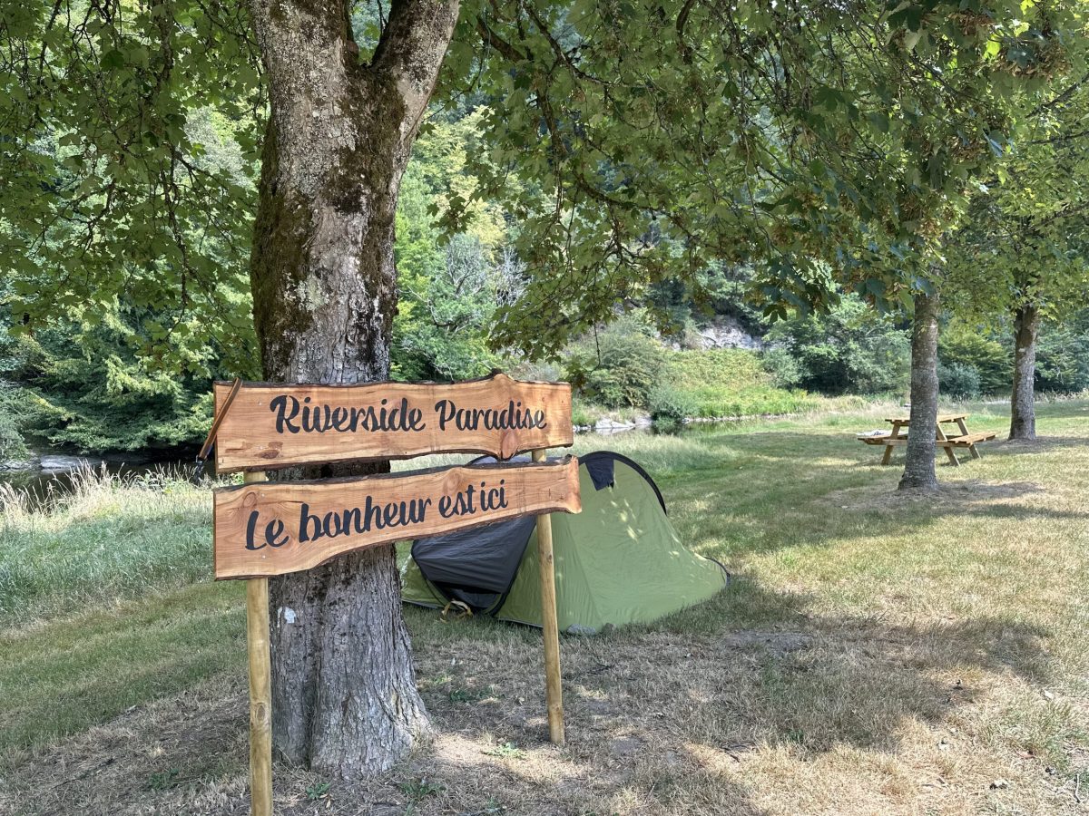 Wooden signpost reading 'Riverside Paradise' and 'Le bonheur existe' near trees in Bouillon