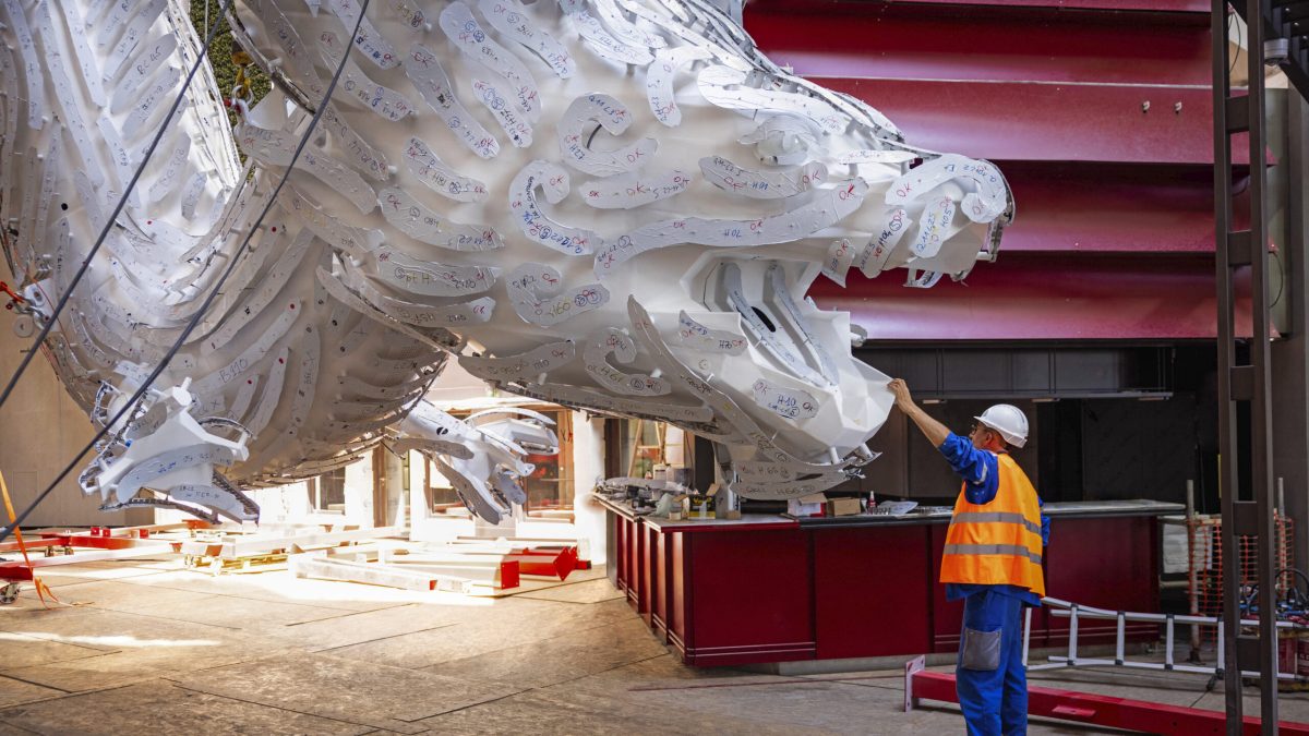 Worker inspecting massive white illuminated dragon sculpture being installed on MSC World Asia cruise ship