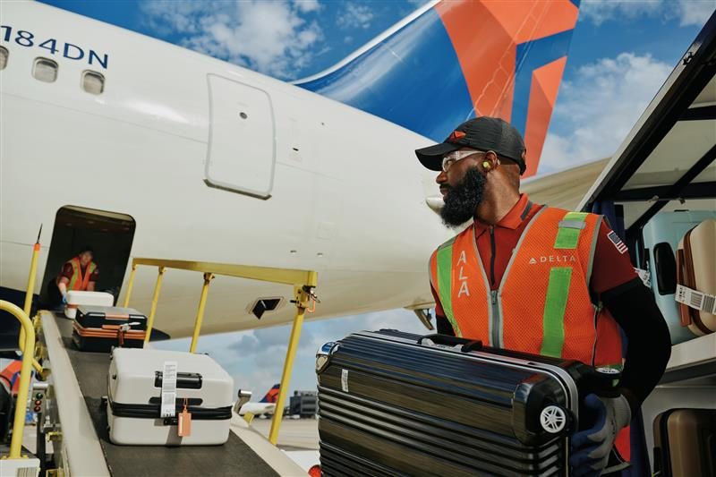 Ground crew member loading a carry-on suitcase into an airplane cargo hold