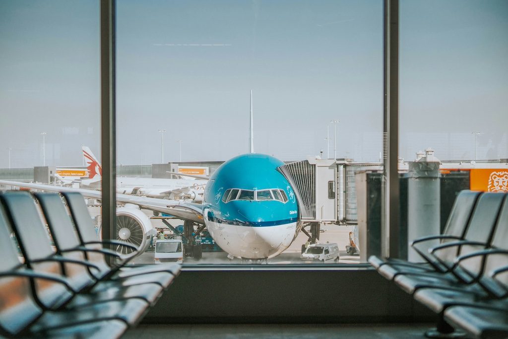 Blue airplane viewed through airport terminal window with empty seating in foreground